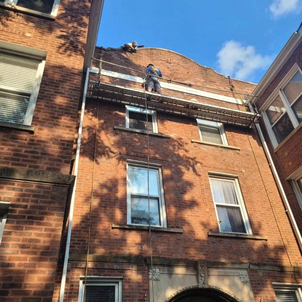 Worker on ropes performing tuckpointing on a multi-story Chicago brick building